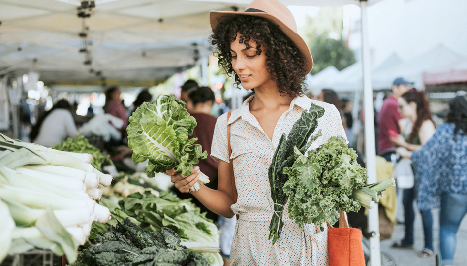 A woman decides between two batches of kale at the farmers market.