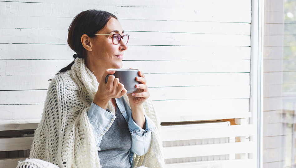 A woman sips a cup of tea on her front porch while strategizing her goals.