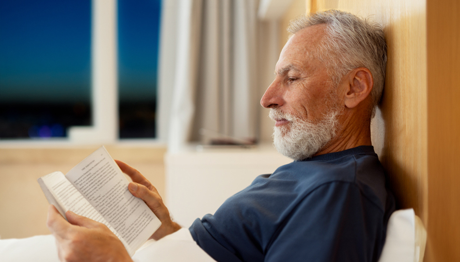 A man reads a novel in bed to wind down before falling asleep.