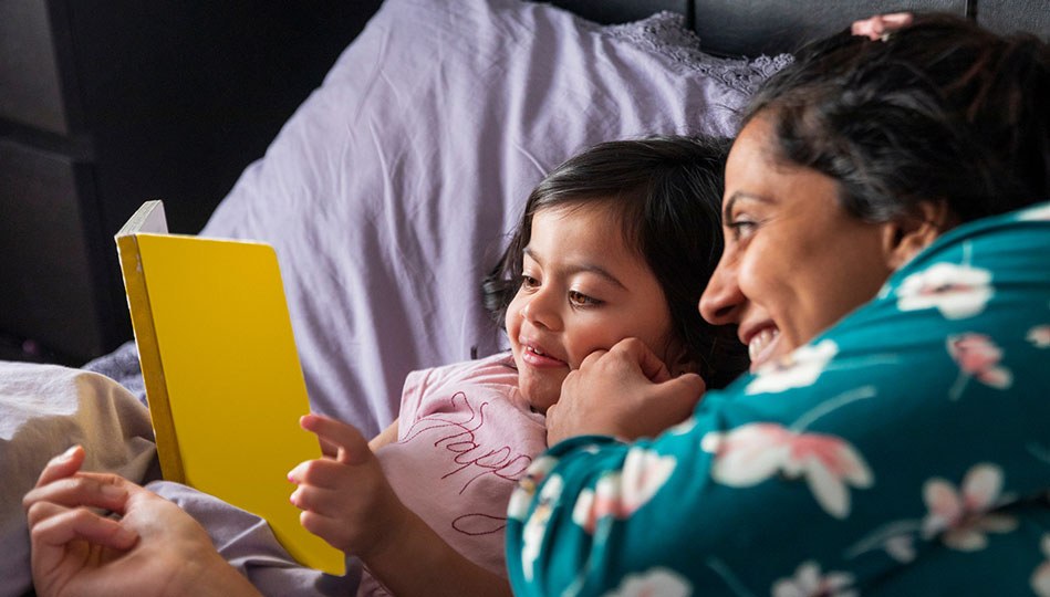 A mother tucks her child into bed to read a book to ease into the daylight savings time shift.