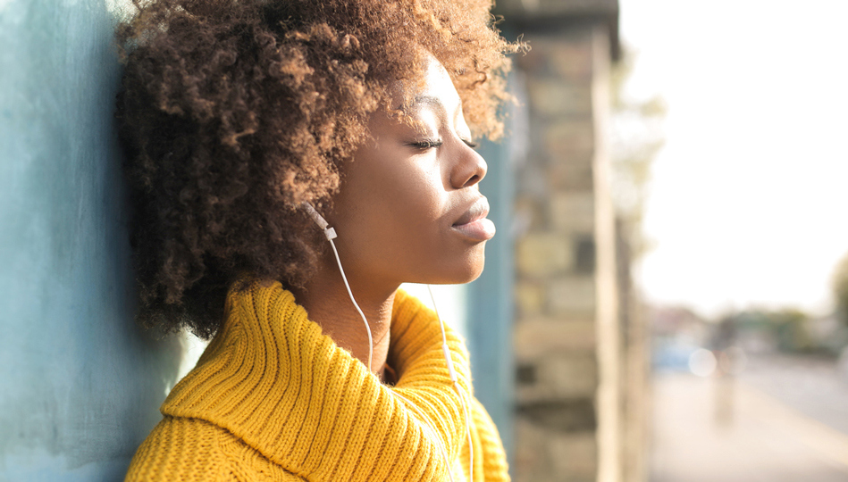 A woman takes 10 minutes out of her workday to practice deep breathing outside while listening to music through her headphones.
