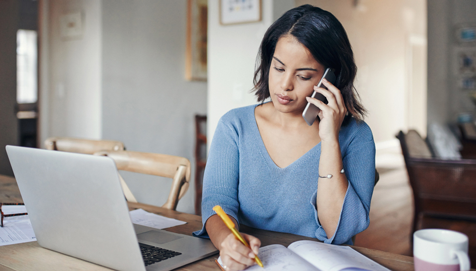 A woman speaks with a MOBE Pharmacist on the phone while taking notes on her medications.