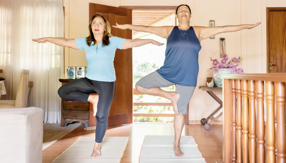 Two women practice yoga in the living room of a house.