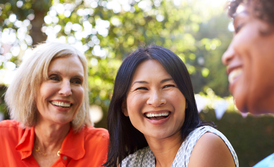 3 women laugh mid-conversation while sitting in the park.