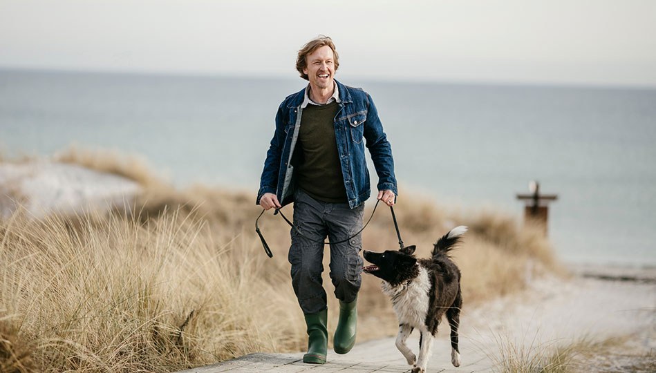 A man takes his dog for a walk on the beach.