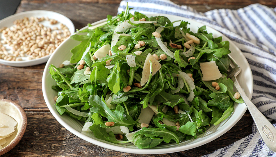 A bed of fresh arugula with shredded cheese and capers on top.