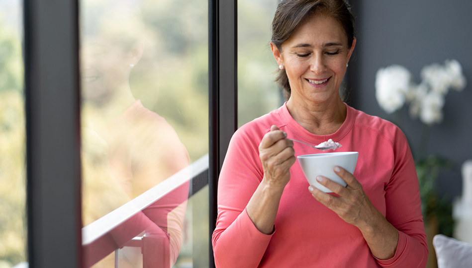 A woman steps away from her TV to eat her bowl of yogurt and be mindful about her meal.