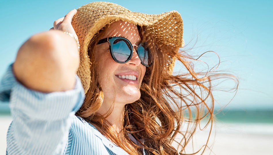 A woman protects her skin at the beach by wearing a sunhat and sunglasses.