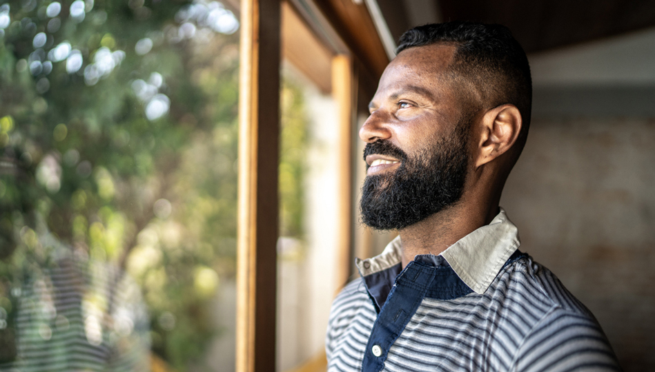 A man gazes out his window onto a bright sunny day.