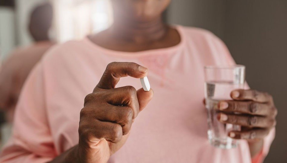 A woman manages her meds by taking her dose in the morning with a glass of water as prescribed by her MOBE Pharmacist.