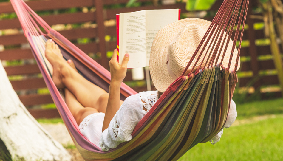 A woman reads a book while laying in a hammock.