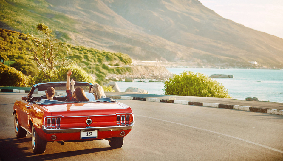 A group of friends ride down the California coast in a convertible.
