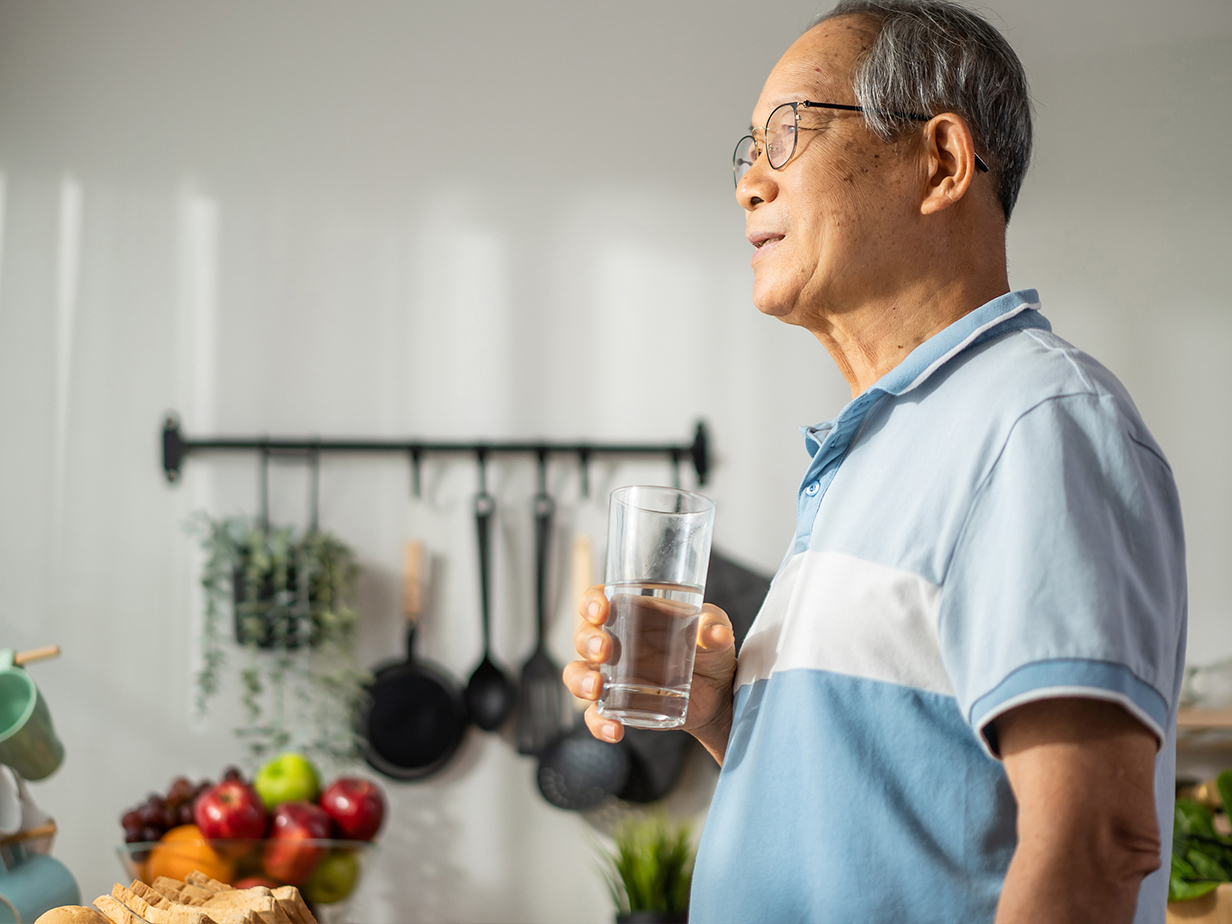 Man holding a glass of water and looking off into the distance.