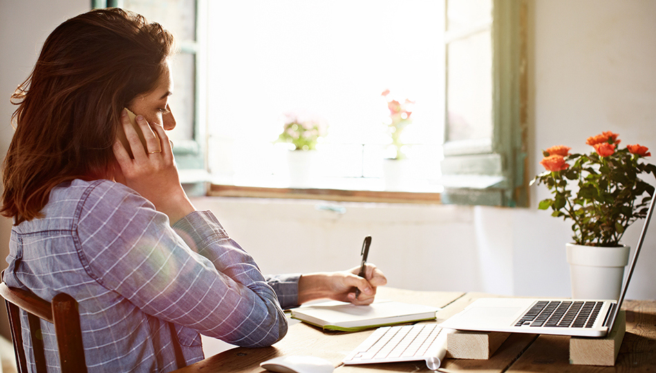 A woman speaks on the phone while taking notes about her medications.